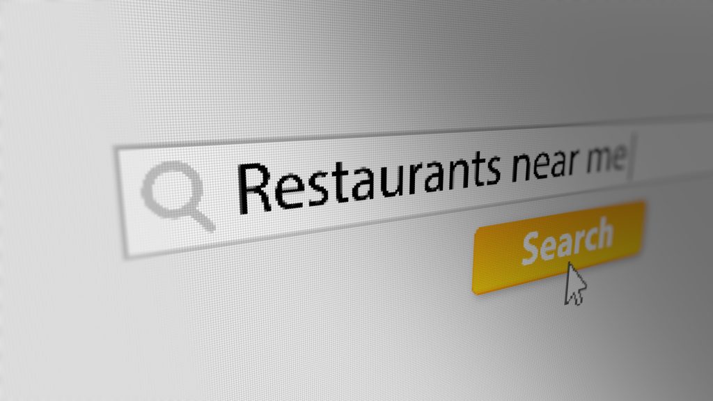 Search for restaurants near me on a computer screen with a yellow search button and a cursor.